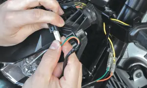 Ręce łączą przewody, pokazując, jak podłączyć kierunkowskazy LED w motocyklu. Pomarańczowy i zielony kabel są przygotowywane do połączenia.