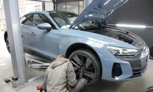 Mechanik pracuje przy niebieskim Audi na podnośniku. Zastanawiasz się, ile trwa wymiana opon z wyważeniem?