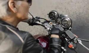 Ręka w rękawiczce motocyklisty na kierownicy, przygotowująca się do wymiany stacyjki. Widoczne zegary i przełączniki.
