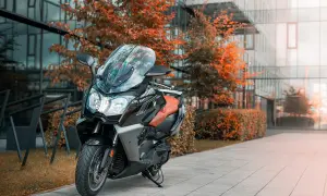 Elegancki skuter BMW C 650 GT z brązową kanapą stoi przed nowoczesnym budynkiem, otoczony jesiennymi drzewami.