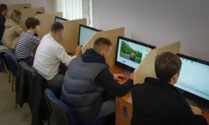 Ludzie siedzą przy komputerach, rozwiązując testy. Zastanawiają się, ile trzeba mieć punktów, żeby zdać egzamin teoretyczny.