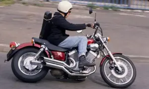 Mężczyzna w kasku jedzie na czerwonym motocyklu Yamaha Virago, z futerałem na instrumenty muzyczne na plecach.