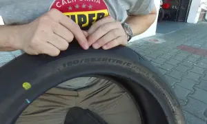 Ręce wskazują na oznaczenia na oponie motocyklowej, pomagając zrozumieć, jak dobrać opony. Widoczny rozmiar 180/55ZR17.