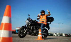 Szczęśliwa motocyklistka z radością prezentuje swoje nowe prawo jazdy kat A, siedząc na motorze na placu manewrowym.