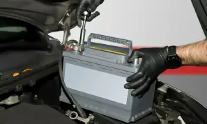 Mechanik w czarnych rękawiczkach wymienia akumulator kwasowy w samochodzie. To pierwszy krok do tego, jak zregenerować akumulator kwasowy.