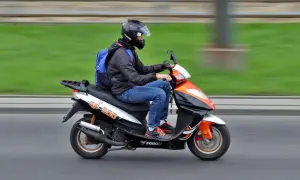 Mężczyzna w kasku i niebieskim plecaku jedzie skuterem. Dowód osobisty wystarczy, by legalnie poruszać się tym pojazdem.