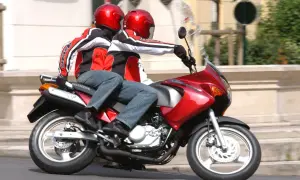 Dwie osoby w czerwonych kaskach i kurtkach jadą na czerwonym motocyklu. To ich pierwsza jazda 125 na dwóch, bez 3 lat doświadczenia.