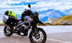 Gotowy na przygodę motocykl szosowy Suzuki V-Strom z sakwami i jaskrawym plecakiem czeka na tle majestatycznych gór i błękitnego nieba.