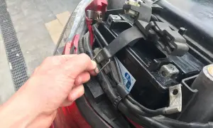 Ręka odkręca mocowanie akumulatora w skuterze. Widać jego umiejscowienie pod siedzeniem.