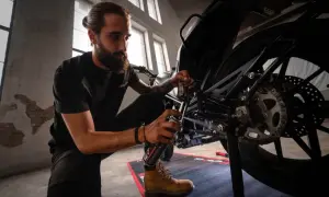 Mężczyzna z brodą konserwuje łańcuch motocykla, pokazując, jak założyć łańcuch.
