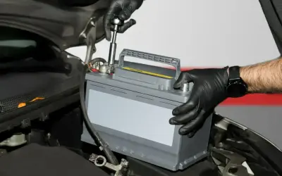 Mechanik w czarnych rękawiczkach wymienia akumulator kwasowy w samochodzie. To pierwszy krok do tego, jak zregenerować akumulator kwasowy.
