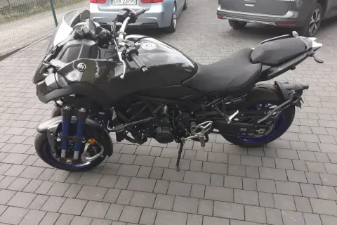 Czarny motocykl Yamaha Niken kat b. na kostce brukowej, z niebieskimi elementami zawieszenia i felg.