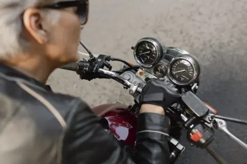 Ręka w rękawiczce motocyklisty na kierownicy, przygotowująca się do wymiany stacyjki. Widoczne zegary i przełączniki.