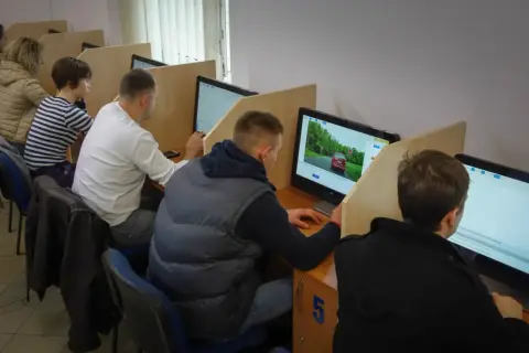 Ludzie siedzą przy komputerach, rozwiązując testy. Zastanawiają się, ile trzeba mieć punktów, żeby zdać egzamin teoretyczny.
