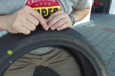 Ręce wskazują na oznaczenia na oponie motocyklowej, pomagając zrozumieć, jak dobrać opony. Widoczny rozmiar 180/55ZR17.