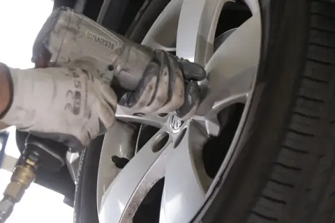Mechanik w białej rękawicy dokręca śruby w feldze, zastanawiając się, ile km wytrzymują opony.