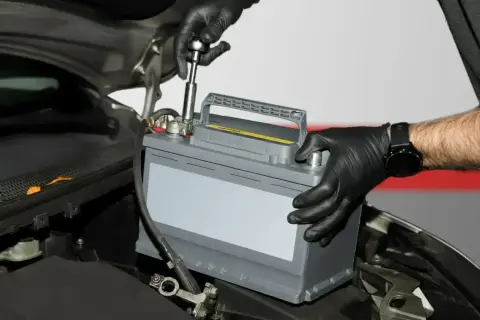 Mechanik w czarnych rękawiczkach wymienia akumulator kwasowy w samochodzie. To pierwszy krok do tego, jak zregenerować akumulator kwasowy.