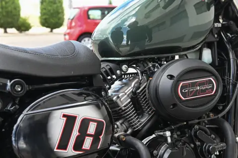 Część motocykla z siedzeniem, silnikiem i napisem "Grand Voyage 125". Numer "18" na błotniku.