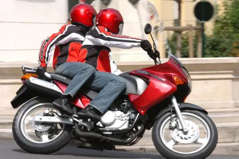 Dwie osoby w czerwonych kaskach i kurtkach jadą na czerwonym motocyklu. To ich pierwsza jazda 125 na dwóch, bez 3 lat doświadczenia.