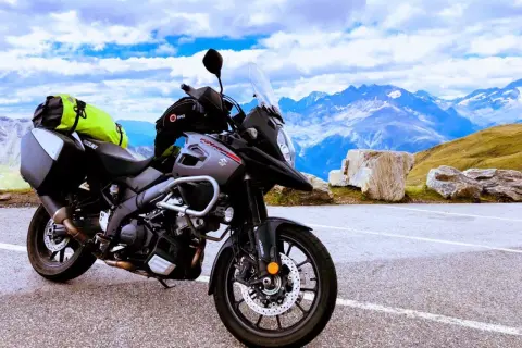 Gotowy na przygodę motocykl szosowy Suzuki V-Strom z sakwami i jaskrawym plecakiem czeka na tle majestatycznych gór i błękitnego nieba.