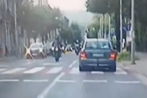 Motocyklista wykonuje jazdę na jednym kole, ryzykując mandat. Samochód jedzie przed nim.