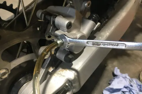 Wymiana płynu hamulcowego w motocyklu. Klucz nasadowy odkręca odpowietrznik zacisku hamulcowego, przez który spływa stary płyn.