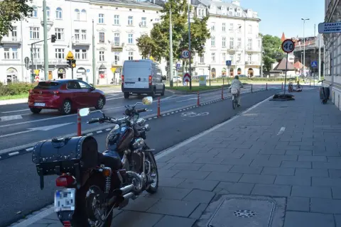 Motocykl zaparkowany na chodniku, obok ścieżki rowerowej. W tle samochody i budynki.