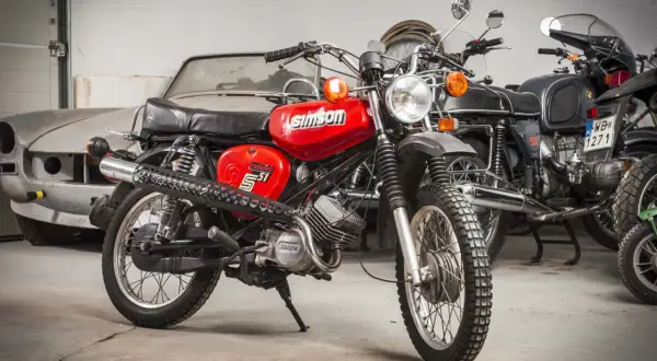 Czerwony Simson S51 Enduro, z widocznymi danymi technicznymi na baku. Obok inne motocykle i stary samochód.