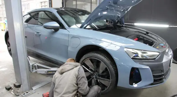 Mechanik pracuje przy niebieskim Audi na podnośniku. Zastanawiasz się, ile trwa wymiana opon z wyważeniem?