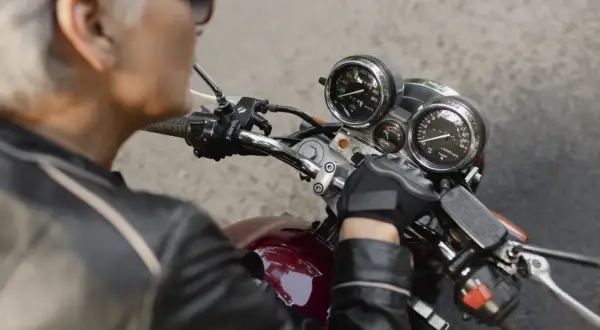 Ręka w rękawiczce motocyklisty na kierownicy, przygotowująca się do wymiany stacyjki. Widoczne zegary i przełączniki.