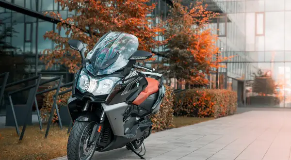 Elegancki skuter BMW C 650 GT z brązową kanapą stoi przed nowoczesnym budynkiem, otoczony jesiennymi drzewami.