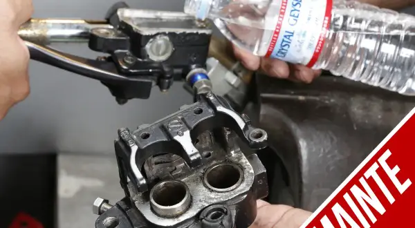 Ręce montują zacisk hamulcowy motocykla, przygotowując go do momentu dokręcania jarzma zacisku. W tle widać zbiorniczek płynu hamulcowego.
