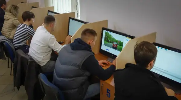 Ludzie siedzą przy komputerach, rozwiązując testy. Zastanawiają się, ile trzeba mieć punktów, żeby zdać egzamin teoretyczny.