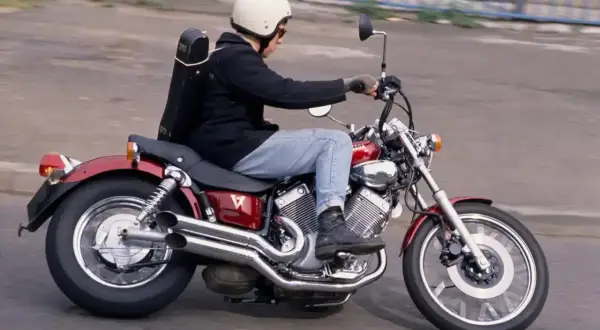 Mężczyzna w kasku jedzie na czerwonym motocyklu Yamaha Virago, z futerałem na instrumenty muzyczne na plecach.