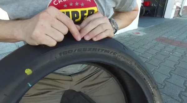 Ręce wskazują na oznaczenia na oponie motocyklowej, pomagając zrozumieć, jak dobrać opony. Widoczny rozmiar 180/55ZR17.
