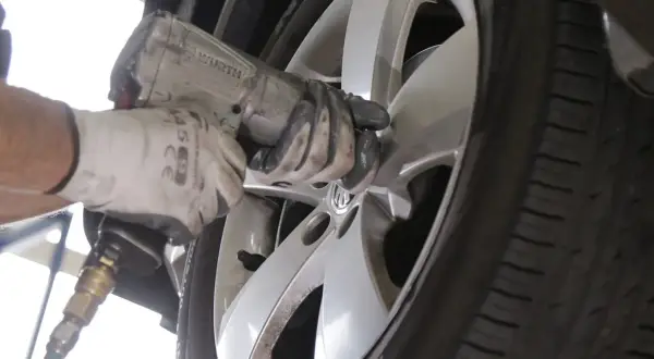 Mechanik w białej rękawicy dokręca śruby w feldze, zastanawiając się, ile km wytrzymują opony.