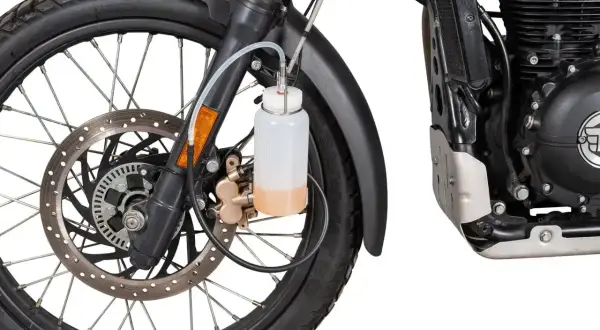 Zbiorniczek z płynem do odpowietrzania hamulców motocykla, podłączony do zacisku hamulcowego przy przednim kole.