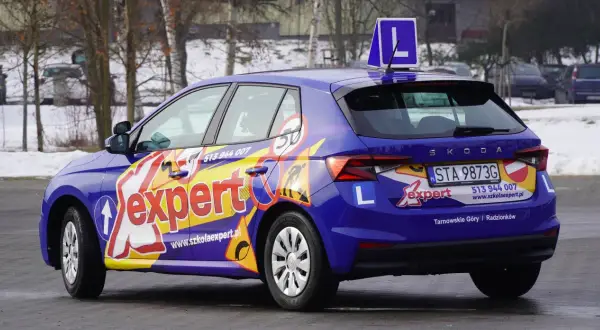 Niebieski samochód szkoleniowy z napisem "expert" i literą "L" na dachu. Zapytaj, ile trwa kurs na prawo jazdy kat A.