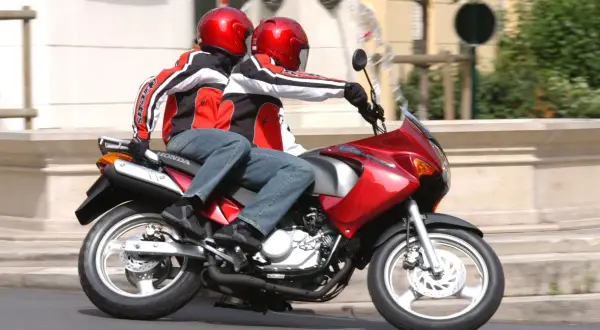 Dwie osoby w czerwonych kaskach i kurtkach jadą na czerwonym motocyklu. To ich pierwsza jazda 125 na dwóch, bez 3 lat doświadczenia.