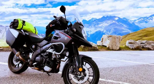 Gotowy na przygodę motocykl szosowy Suzuki V-Strom z sakwami i jaskrawym plecakiem czeka na tle majestatycznych gór i błękitnego nieba.