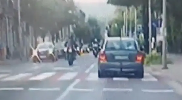 Motocyklista wykonuje jazdę na jednym kole, ryzykując mandat. Samochód jedzie przed nim.