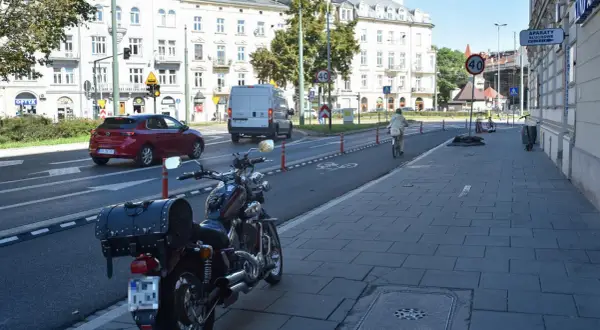 Motocykl zaparkowany na chodniku, obok ścieżki rowerowej. W tle samochody i budynki.
