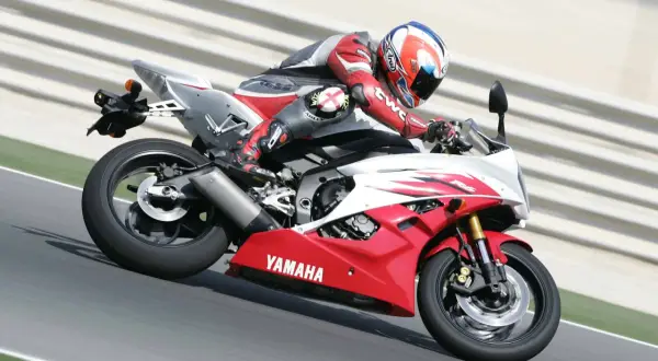 Motocyklista w czerwonym kombinezonie śmiga na torze Yamahą R6. Od ilu lat można robić prawo jazdy na motor 600? Od 20 lat na kategorię A.