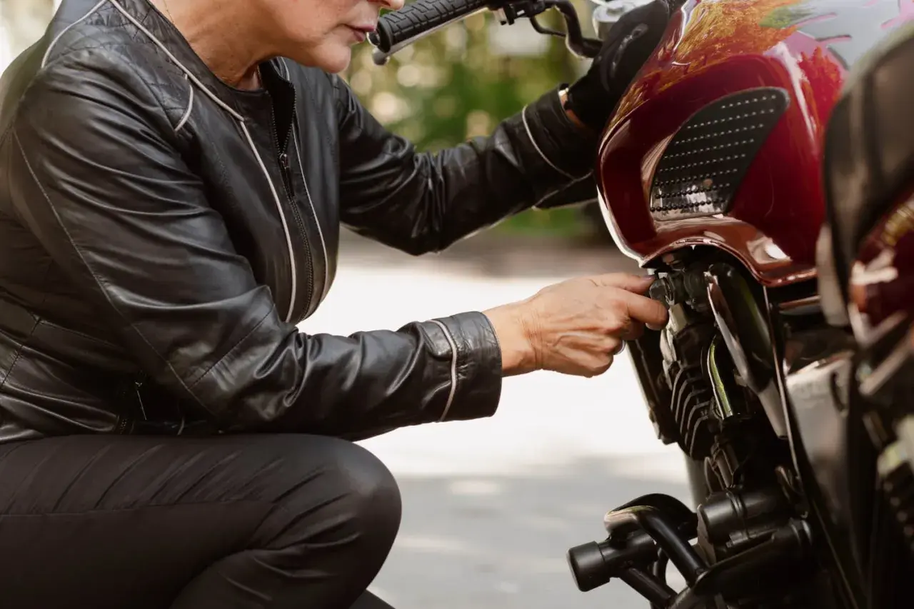 Kobieta w skórzanej kurtce sprawdza regulator napięcia w motocyklu.
