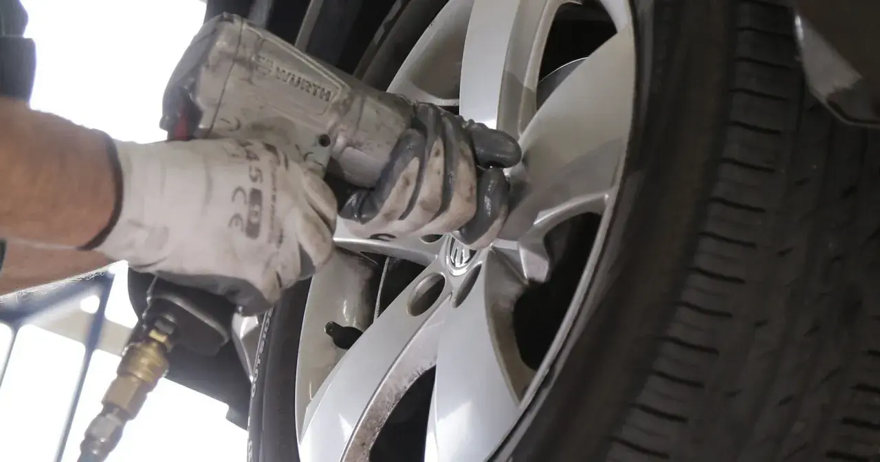 Mechanik w białej rękawicy dokręca śruby w feldze, zastanawiając się, ile km wytrzymują opony.