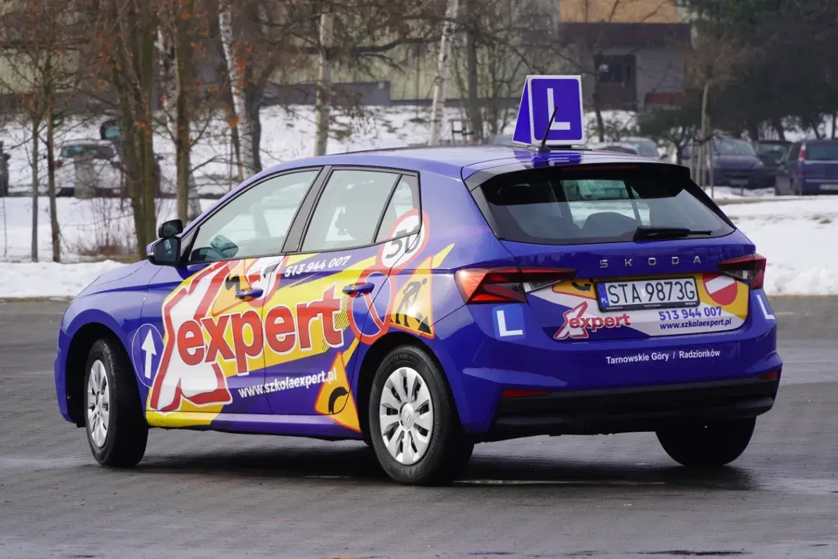 Niebieski samochód szkoleniowy z napisem "expert" i literą "L" na dachu. Zapytaj, ile trwa kurs na prawo jazdy kat A.