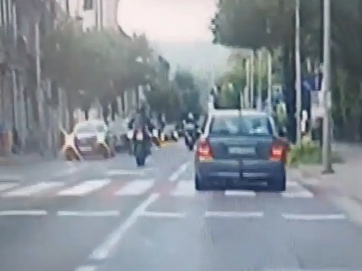 Motocyklista wykonuje jazdę na jednym kole, ryzykując mandat. Samochód jedzie przed nim.