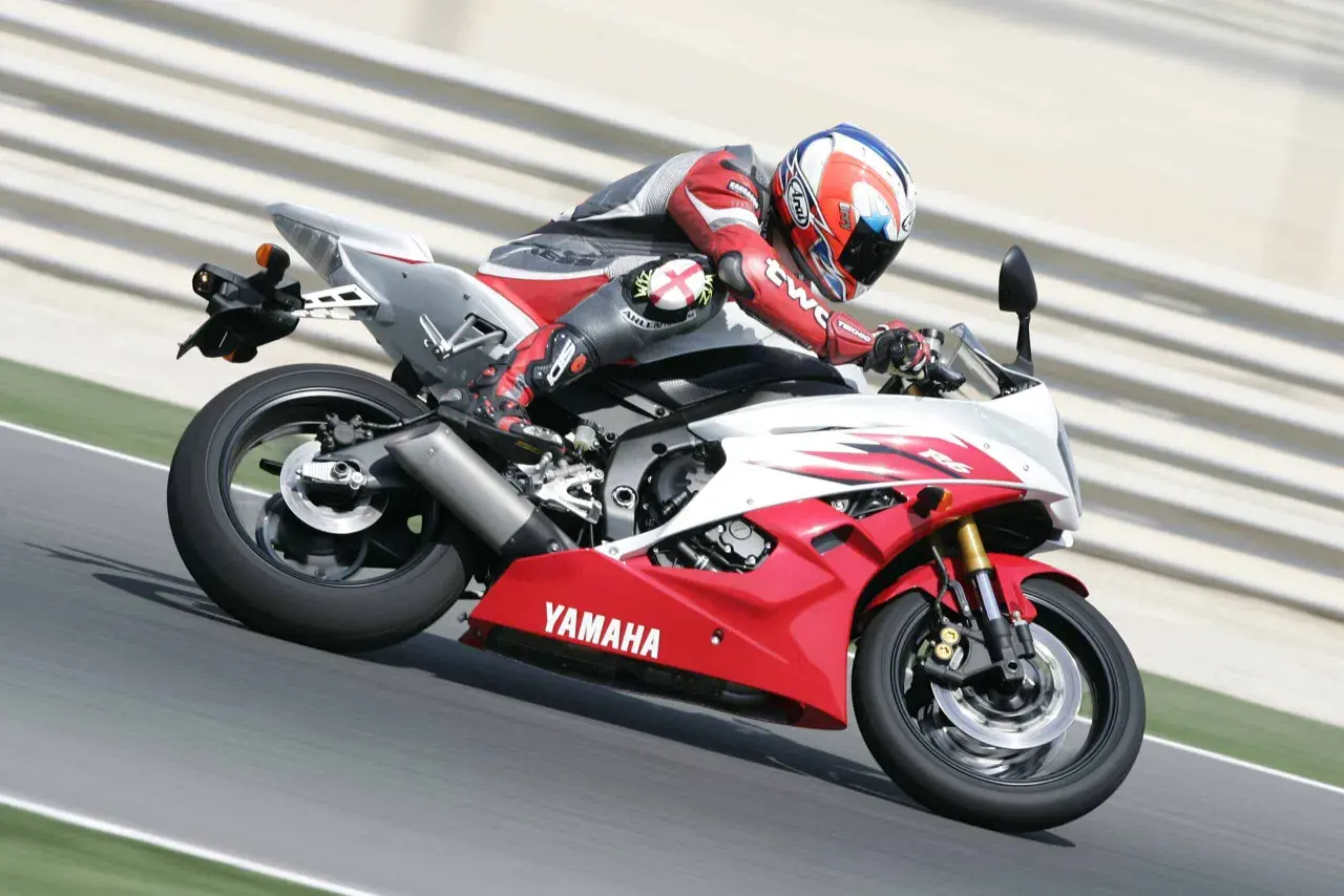 Motocyklista w czerwonym kombinezonie śmiga na torze Yamahą R6. Od ilu lat można robić prawo jazdy na motor 600? Od 20 lat na kategorię A.