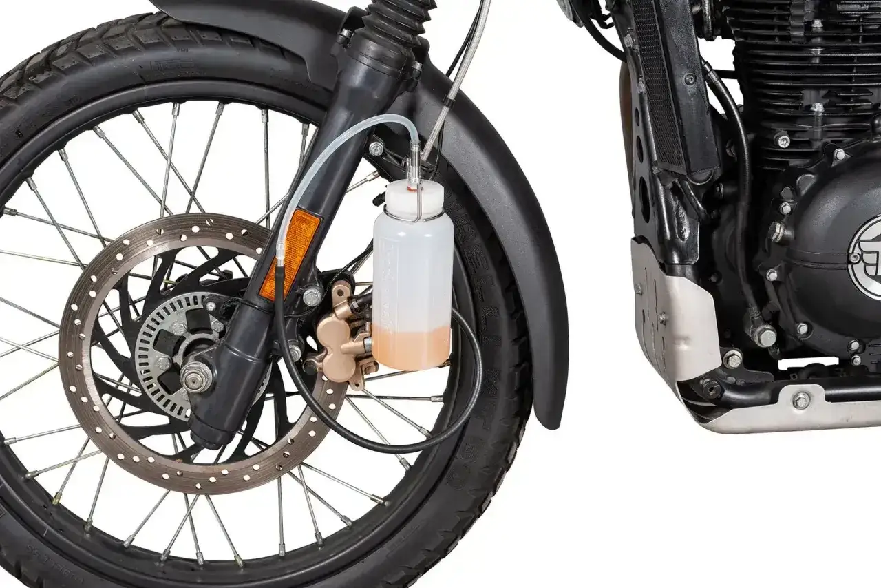 Zbiorniczek z płynem hamulcowym podłączony do zacisku motocykla, sugeruje odpowietrzony układ hamulcowy.