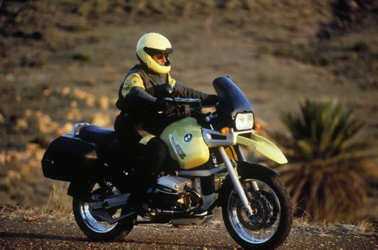 Motocyklista w ż&oacute;łtym kasku na BMW R 1100 RT, jadący po pustynnej drodze. Wady tego modelu to m.in. wysoka cena.